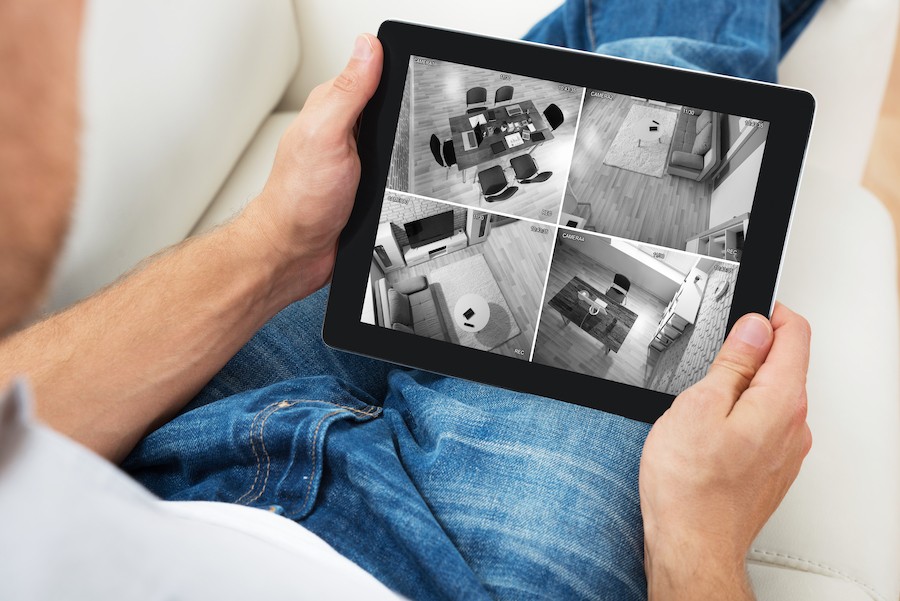 Person monitoring security camera footage from a tablet on their couch.