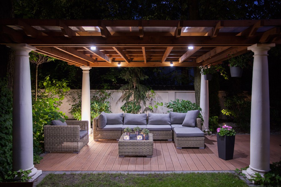 An outdoor deck with seating and a pergola lit up at night.